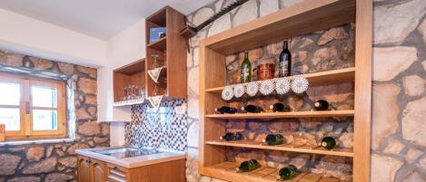 Une cuisine avec des meubles de rangement en bois, un mur en pierre et des étagères où sont disposées des bouteilles de vin et des verres.