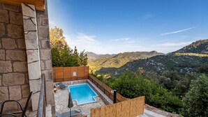 Un patio con paredes de piedra, piscina, mobiliario exterior y vistas a un paisaje montañoso.