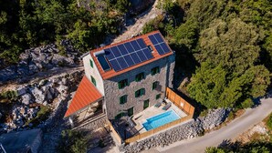 Un edificio de piedra con piscina, paneles solares y techo rojo.