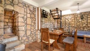 Una habitación con paredes de piedra, una mesa de comedor de madera, sillas y una escalera que sube a una zona superior.