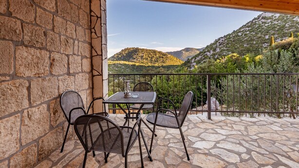 Un patio de piedra con una mesa y sillas, un muro de piedra y vistas a un paisaje montañoso.