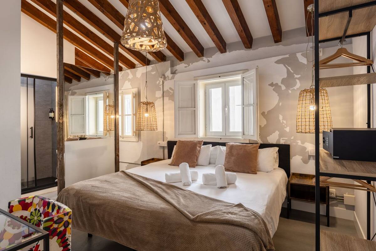 Ein modernes Schlafzimmer mit einem großen Bett, Holzbalken und einer Hängeleuchte.