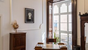 Ein Essbereich mit Holztisch und -stühlen, einer blauen Hängelampe, einem gerahmten Bild an der Wand und einem Fenster mit Blick nach draußen.