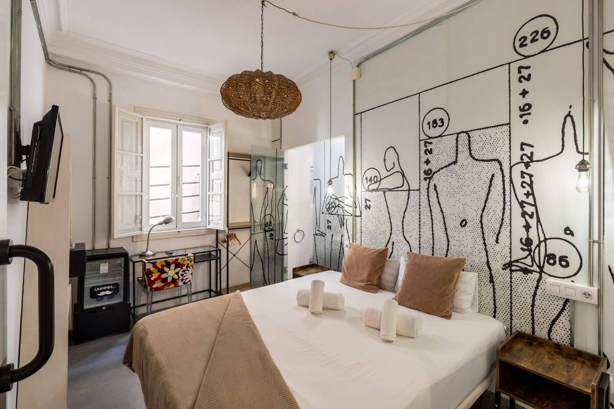 Ein Schlafzimmer mit einem Bett, einem Schreibtisch und einer Wand mit abstrakten Zeichnungen.