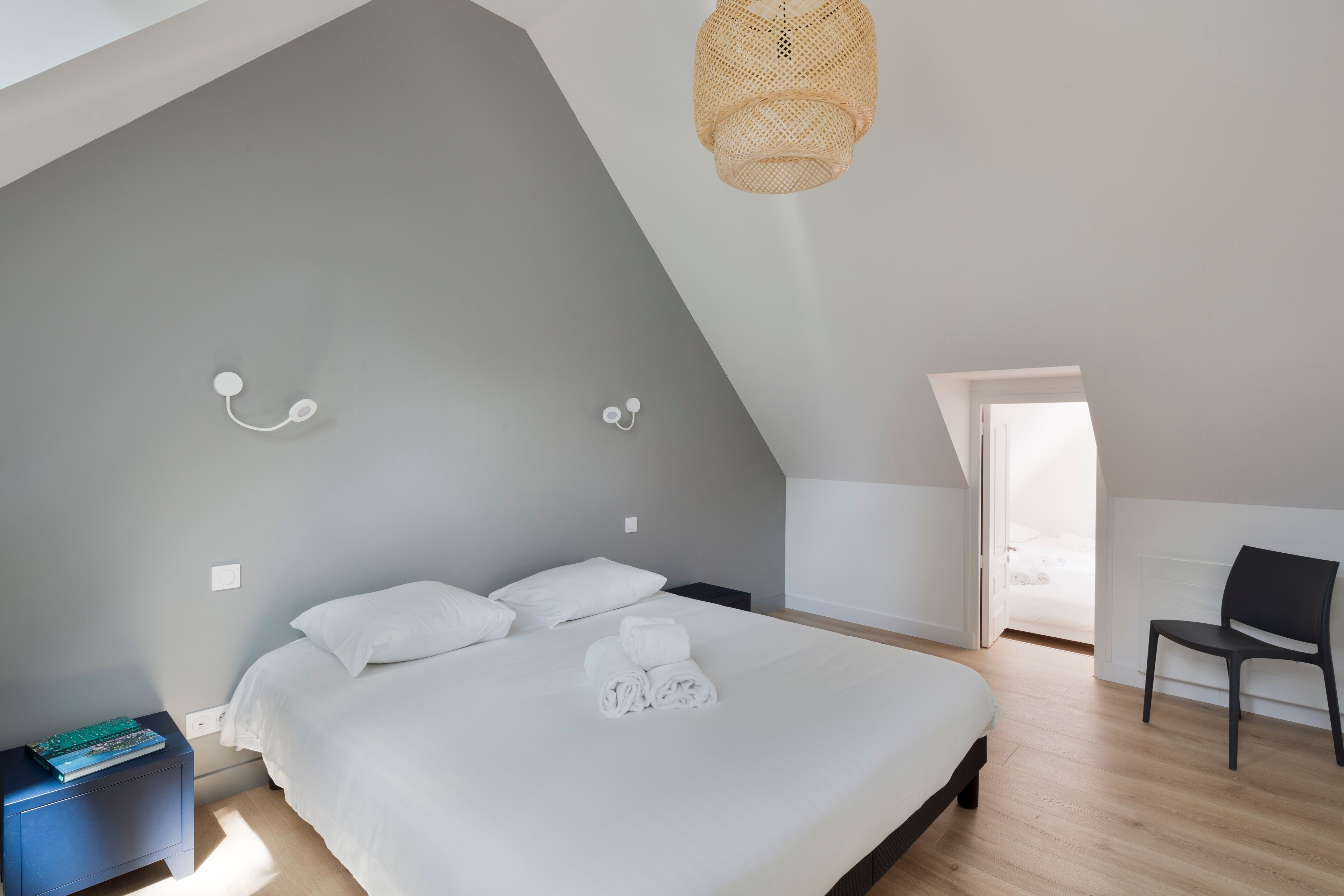 Une chambre à coucher moderne avec un grand lit, une table de chevet, une chaise et un luminaire en matière tressée.