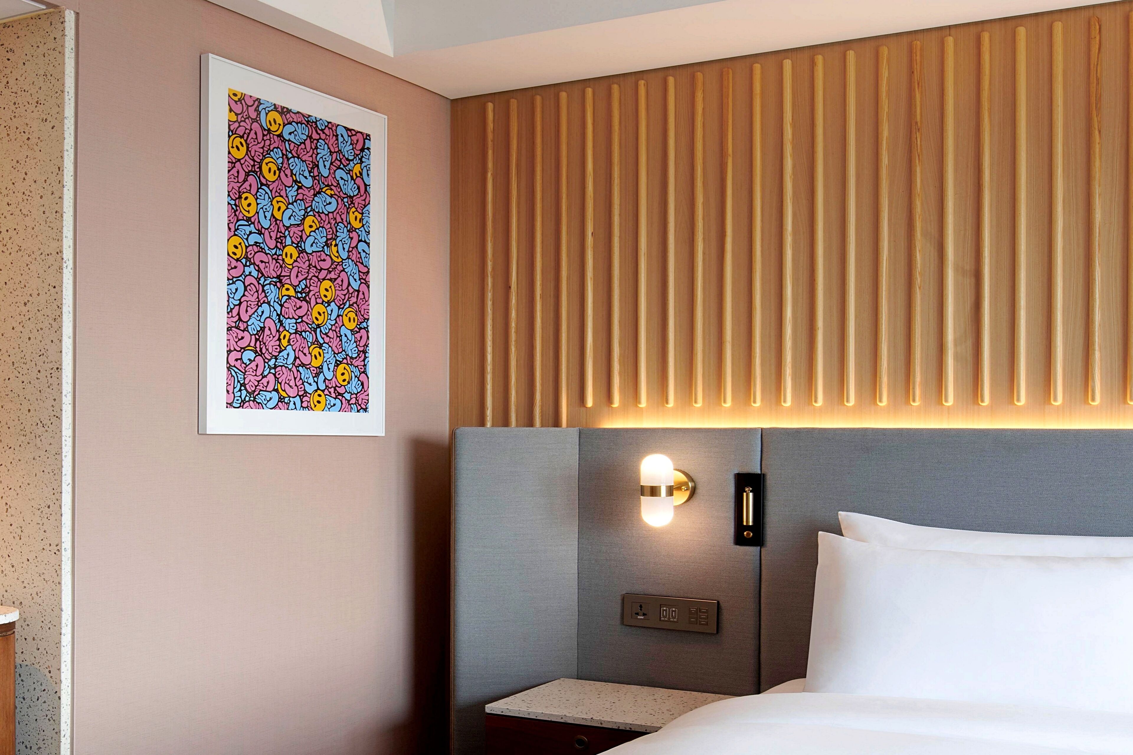 Une chambre d’hôtel avec un lit, une table de chevet, une lampe fixée au mur et un tableau encadré.