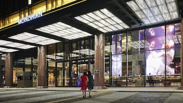 A hotel entrance with a large illuminated sign, glass facade, and a visible seating area outside.