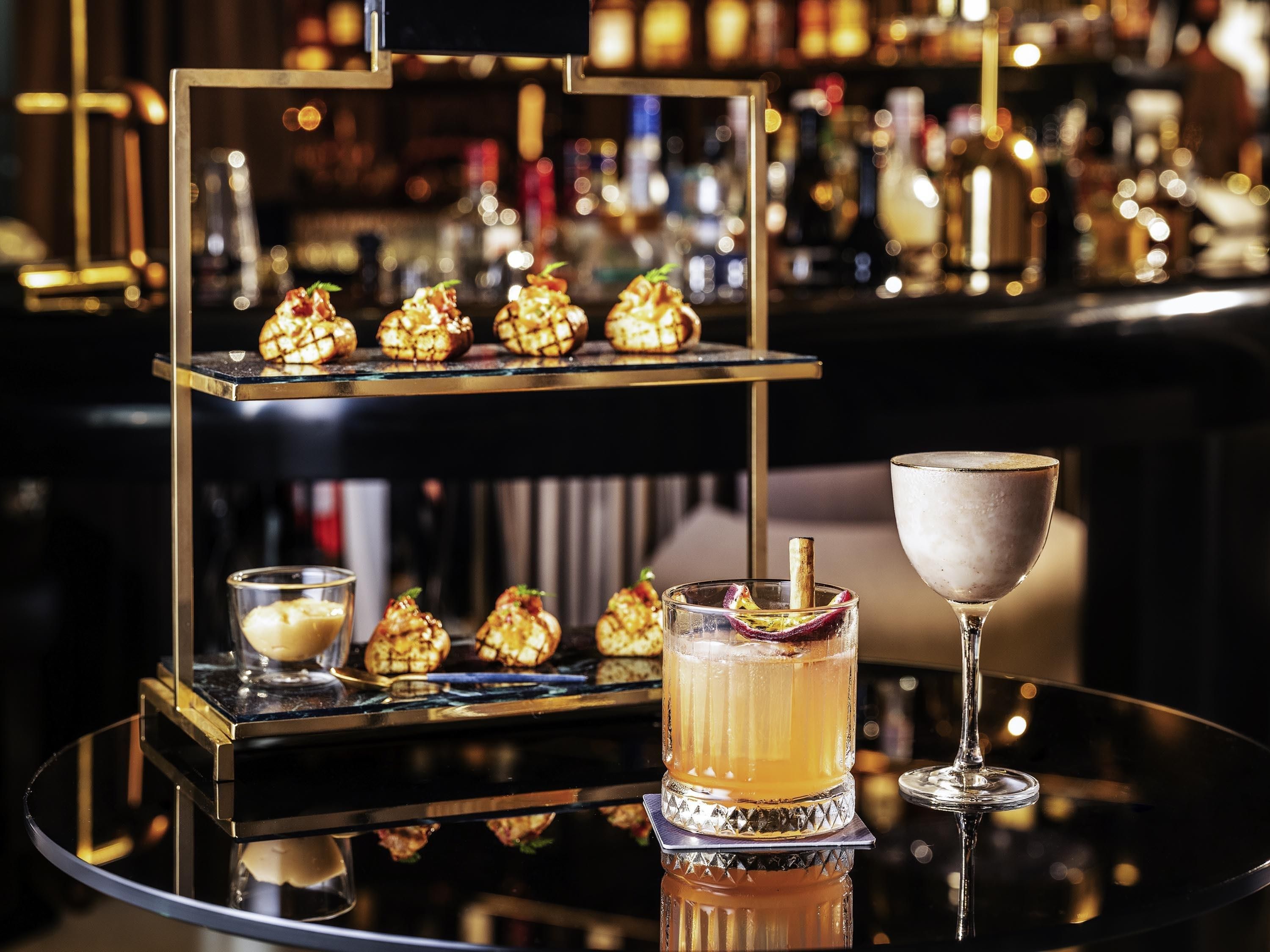 Una zona de bar con una vitrina de postres de dos niveles, una copa de cóctel y un vaso pequeño de una bebida cremosa.