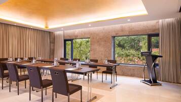 A conference room with a long table, chairs, a podium, and a view of greenery through large windows.