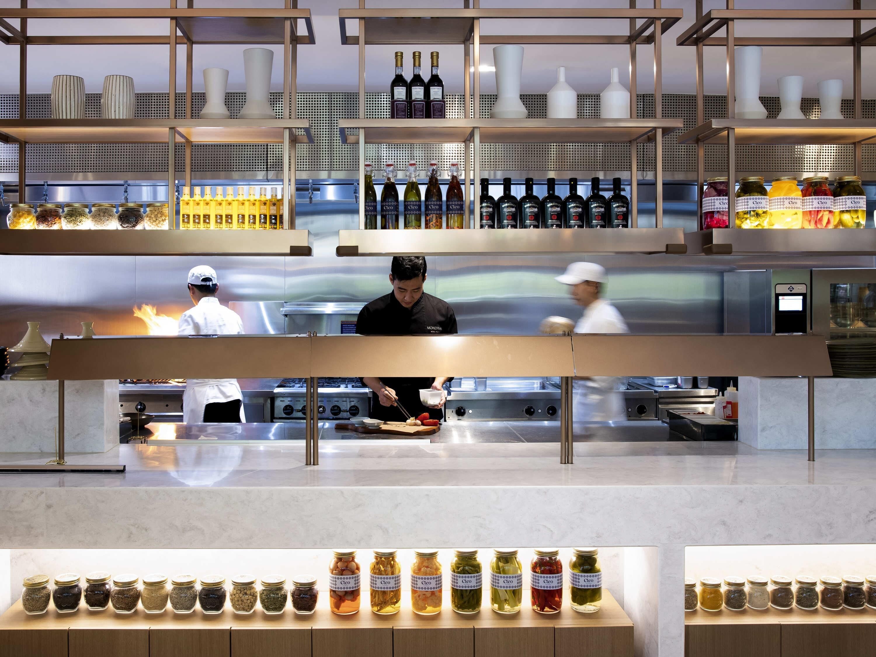 A restaurant with a kitchen area, a display of jars, and bottles on shelves.