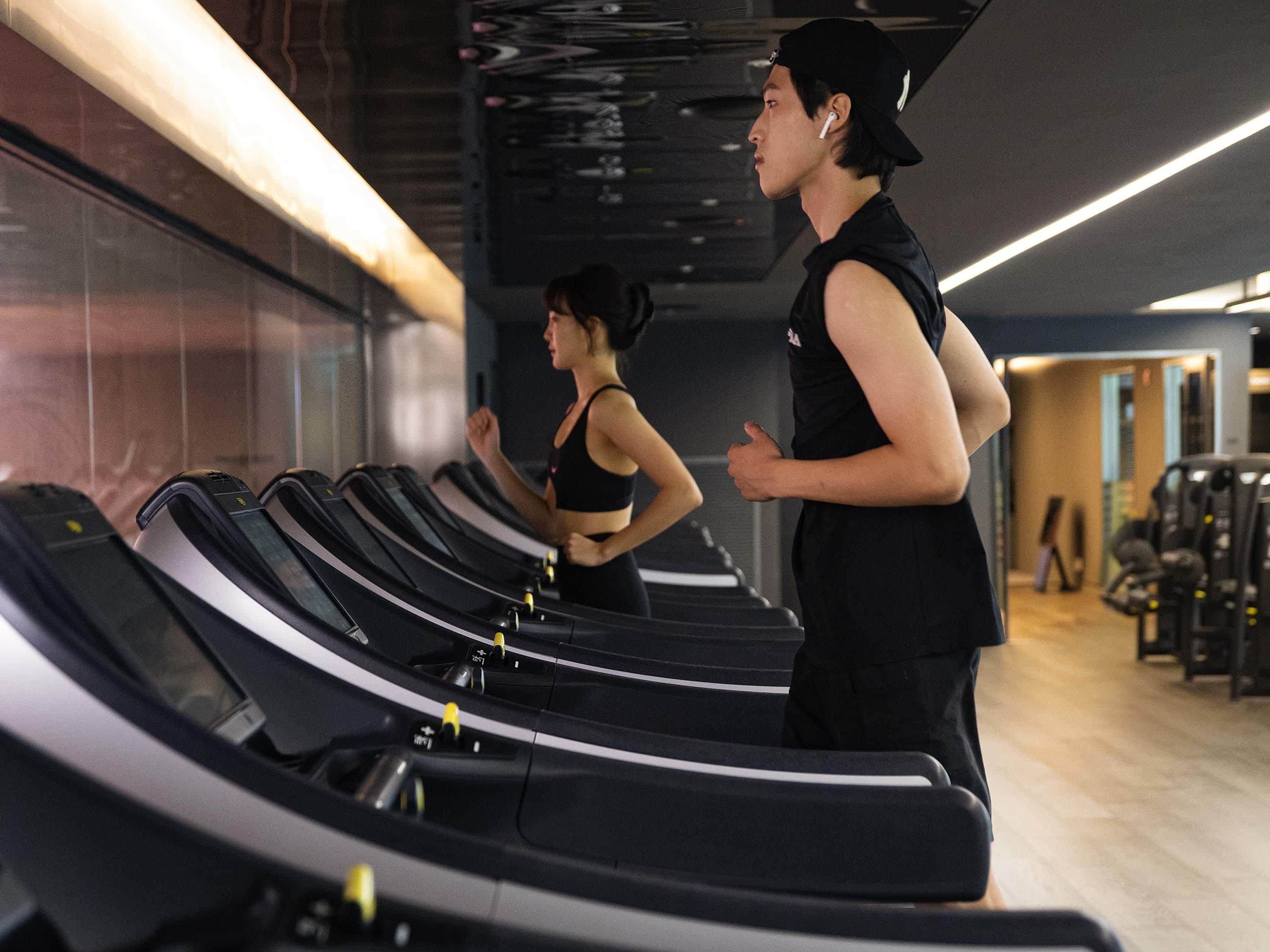 A gym with treadmills, exercise equipment, and a person running.