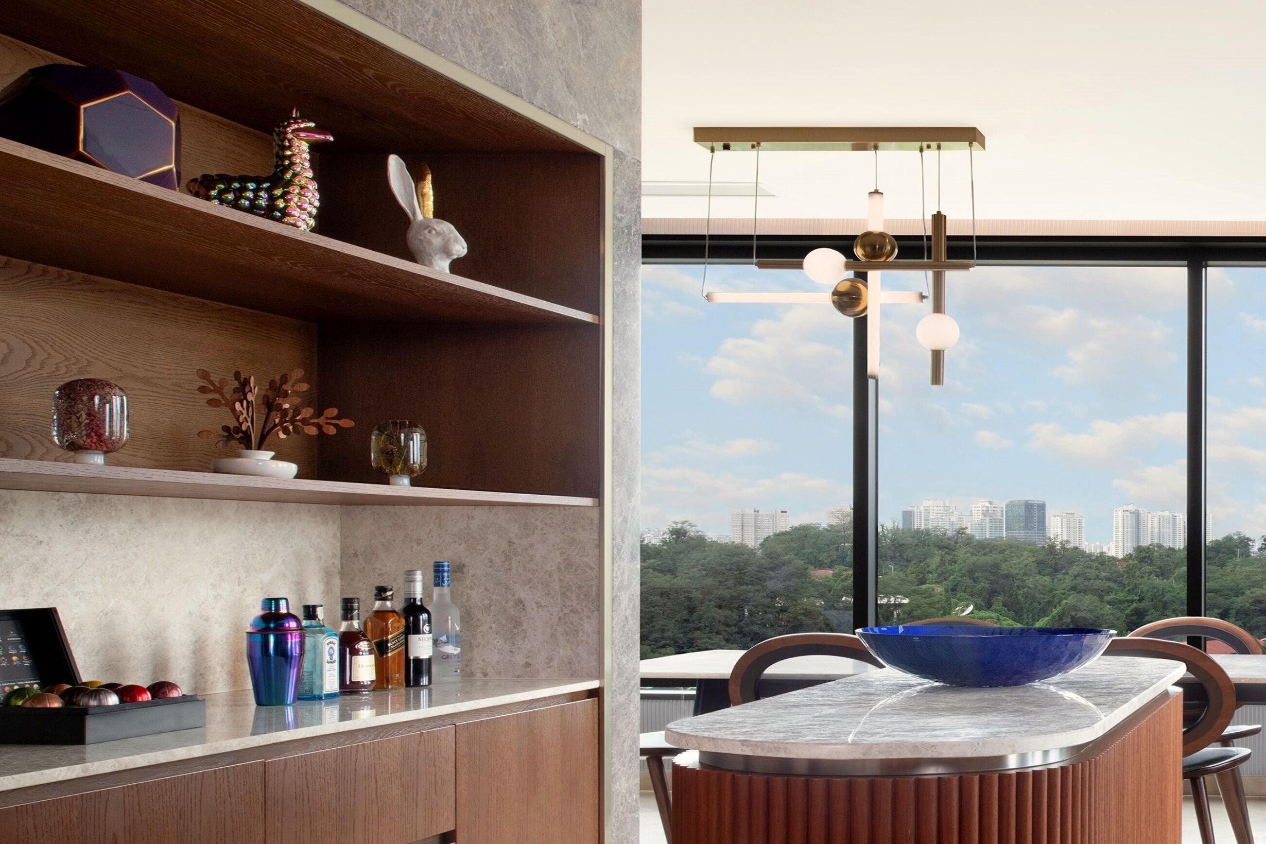 Una cucina moderna con una grande finestra, uno scaffale in legno con oggetti decorativi e un'area pranzo con una ciotola blu sul tavolo.