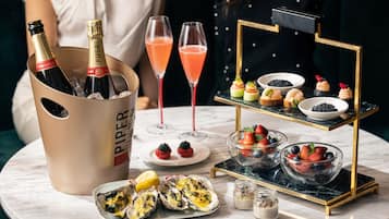 Una mesa con un cubo de champán, dos vasos de cóctel rosado, una bandeja de postres y ostras frescas.