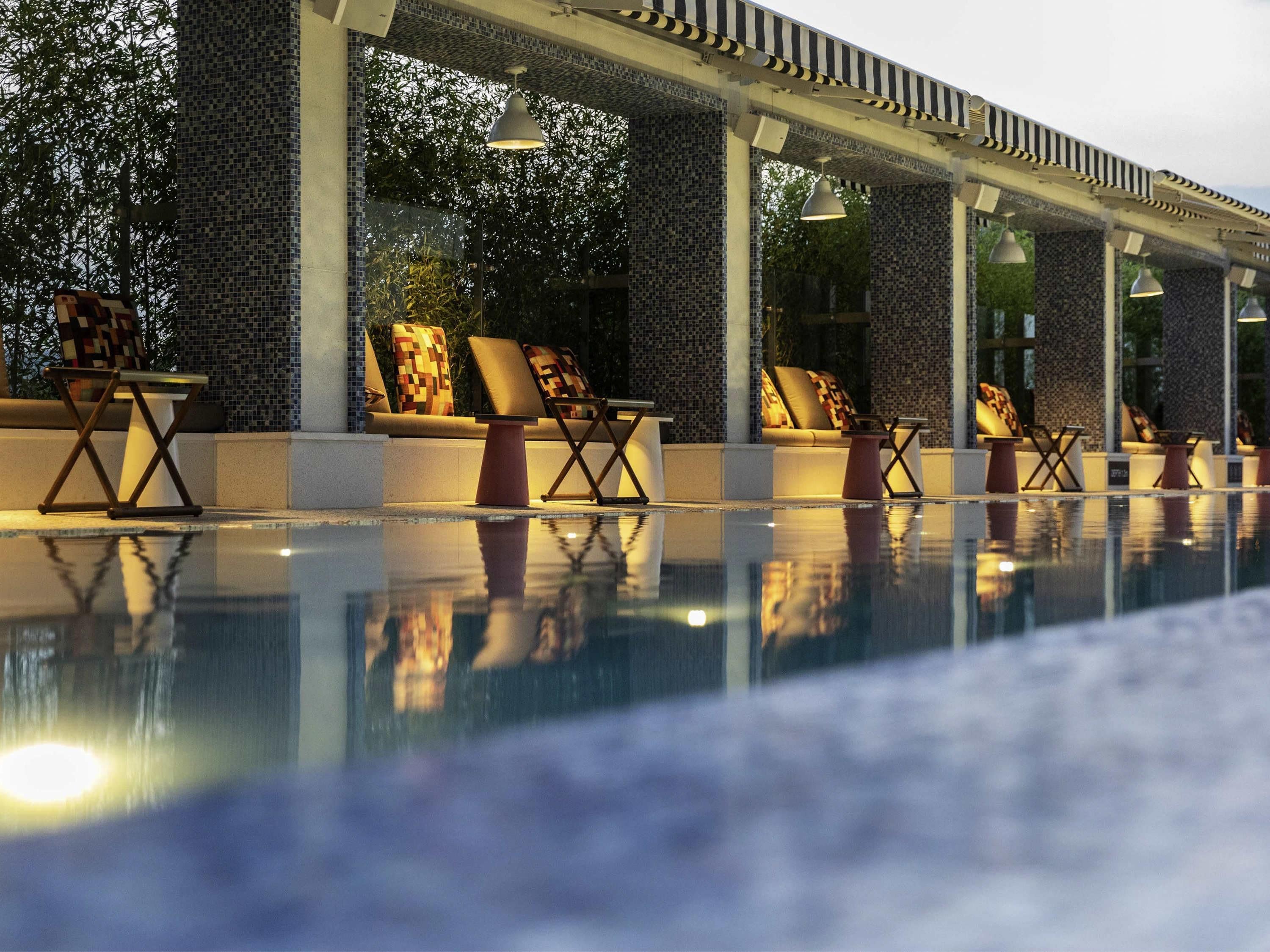 Un espace aménagé au bord de la piscine, avec des chaises longues et un mur recouvert de carreaux.
