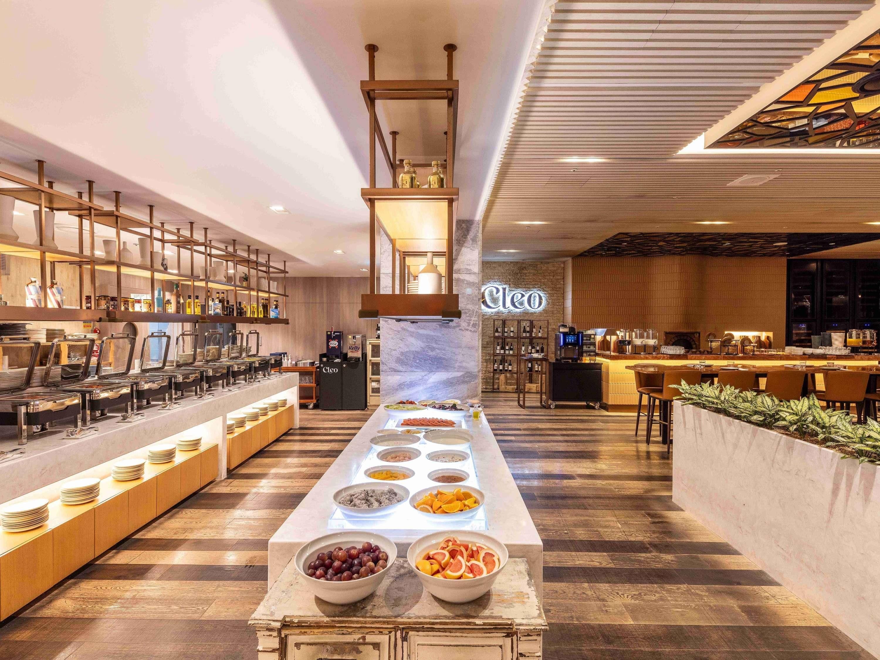 A modern hotel lobby with a long buffet table, a coffee station, and a seating area with a fireplace.