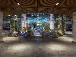 A spacious atrium with a central garden, wooden ceiling panels, and a reflective glass wall.