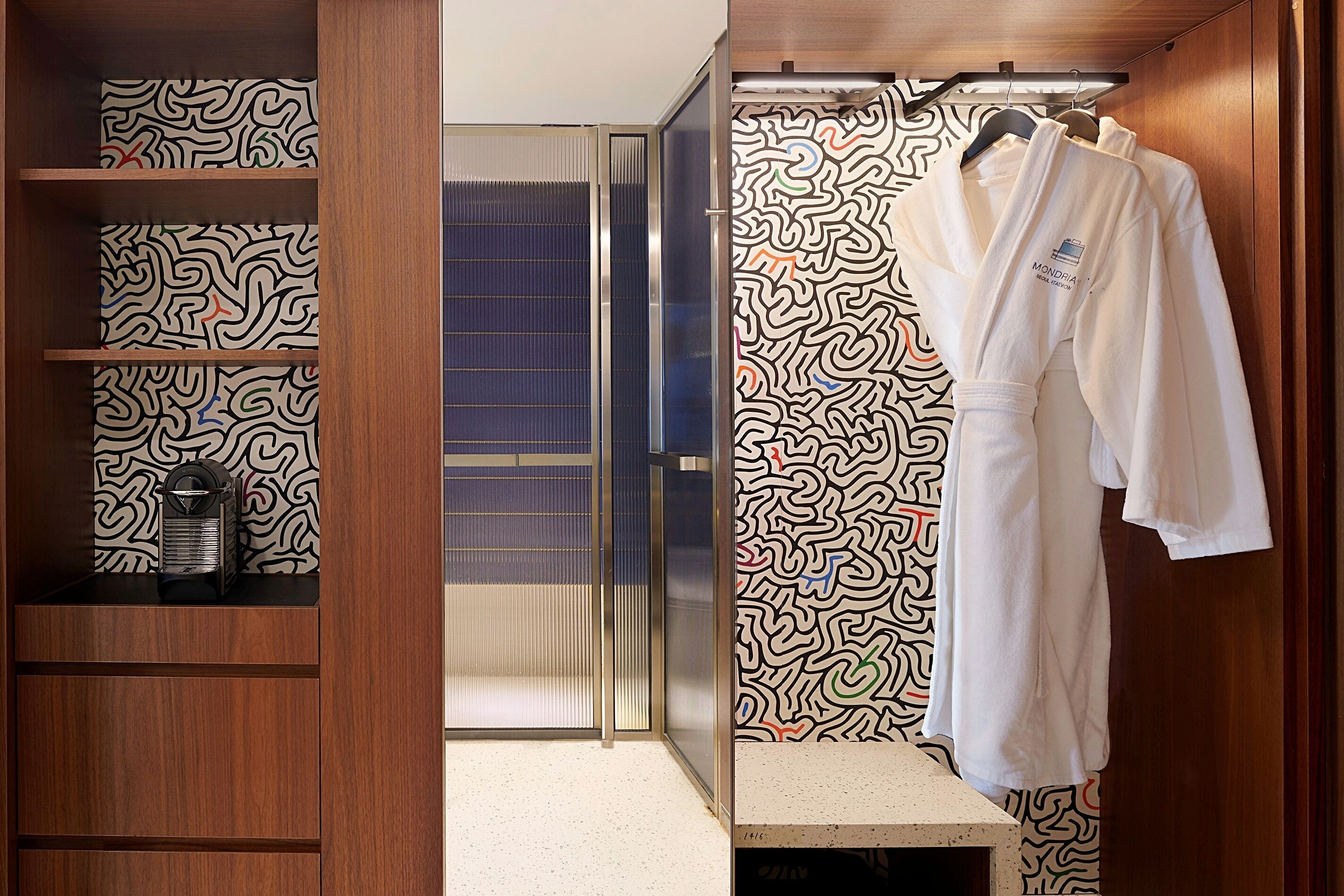 A walk-in closet with patterned wallpaper, a robe hanging on a rack, and a mirror.