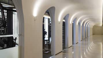 A long, well-lit corridor with arched ceilings and a polished floor, leading to a gym area with exercise equipment.