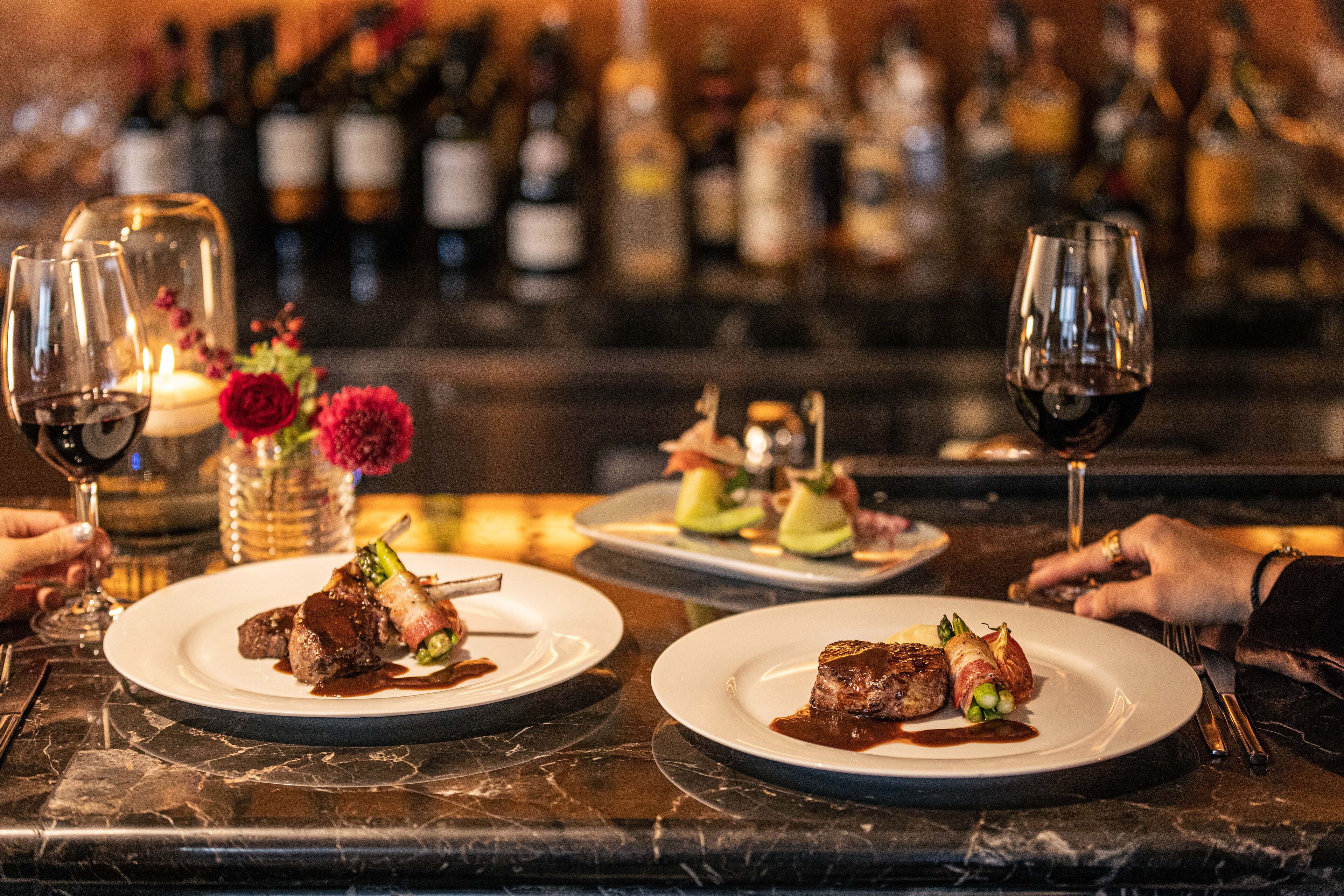 Een restaurantsetting met meerdere borden eten, wijnkannen en een bar met flessen op de achtergrond.