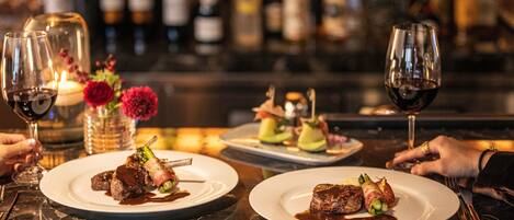 Een restaurantsetting met meerdere borden eten, wijnkannen en een bar met flessen op de achtergrond.