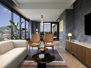 A modern living room with a sofa, two chairs, a coffee table, a TV, and a view of the city. - Mondrian Seoul Itaewon (Seoul)
