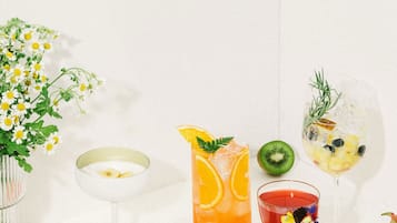 Una mesa con diversas frutas, bebidas y un jarrón de flores.