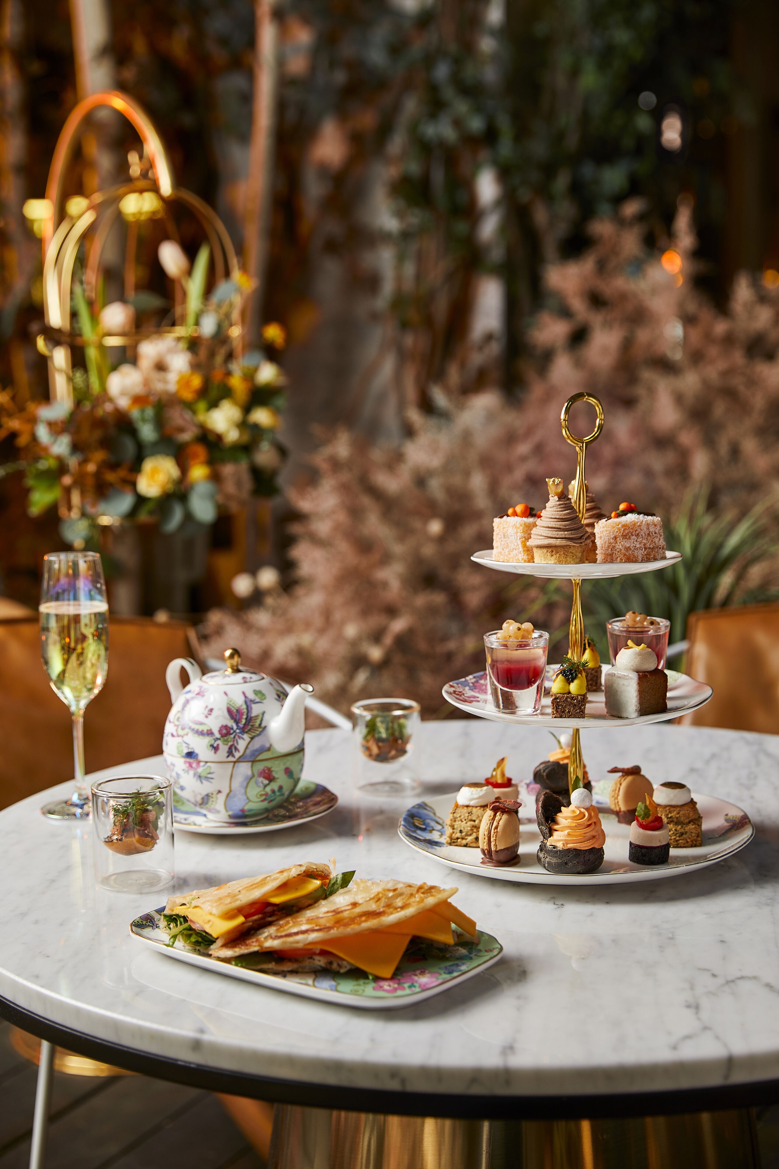 A table set with a variety of desserts and sandwiches, a teapot, and a glass of wine, suggesting a dining experience.