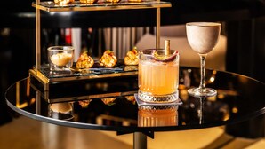 A bar setting with a three-tiered dessert display, a cocktail glass, and a bottle of liquor on a reflective table. - Mondrian Seoul Itaewon (Seoul)