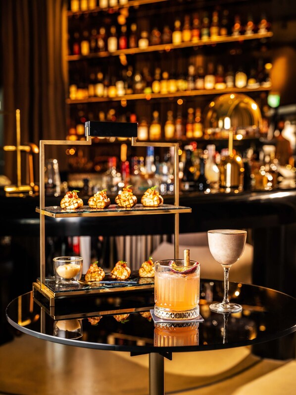 Un ambiente de bar con un pastel de tres niveles, una copa de cóctel y una botella de licor sobre una mesa reflectante.