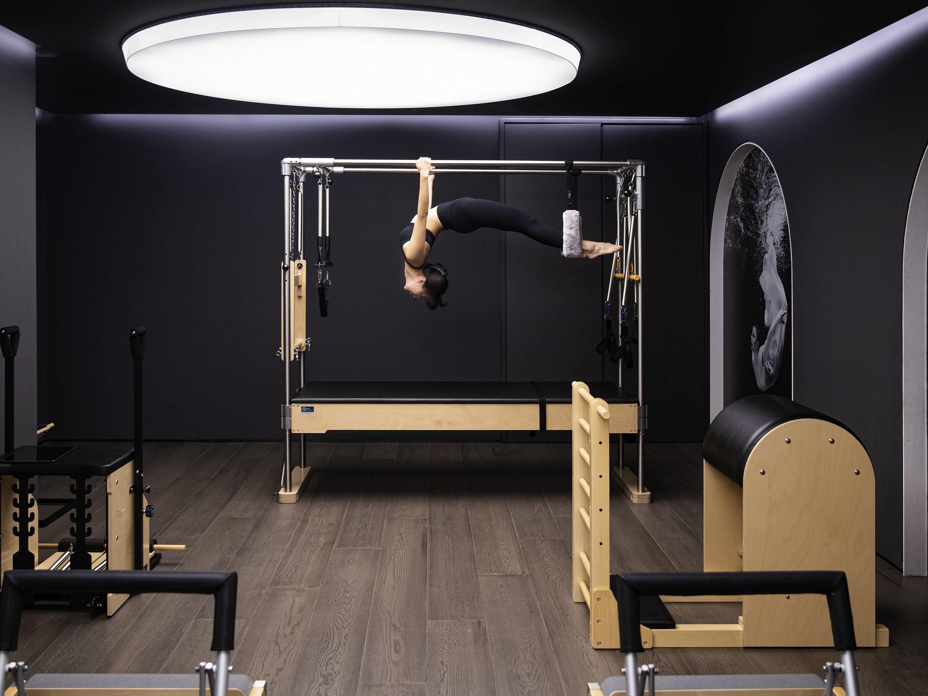 Un estudio de Pilates con piso de madera, un equipo reformador de Pilates y un espejo montado en la pared.