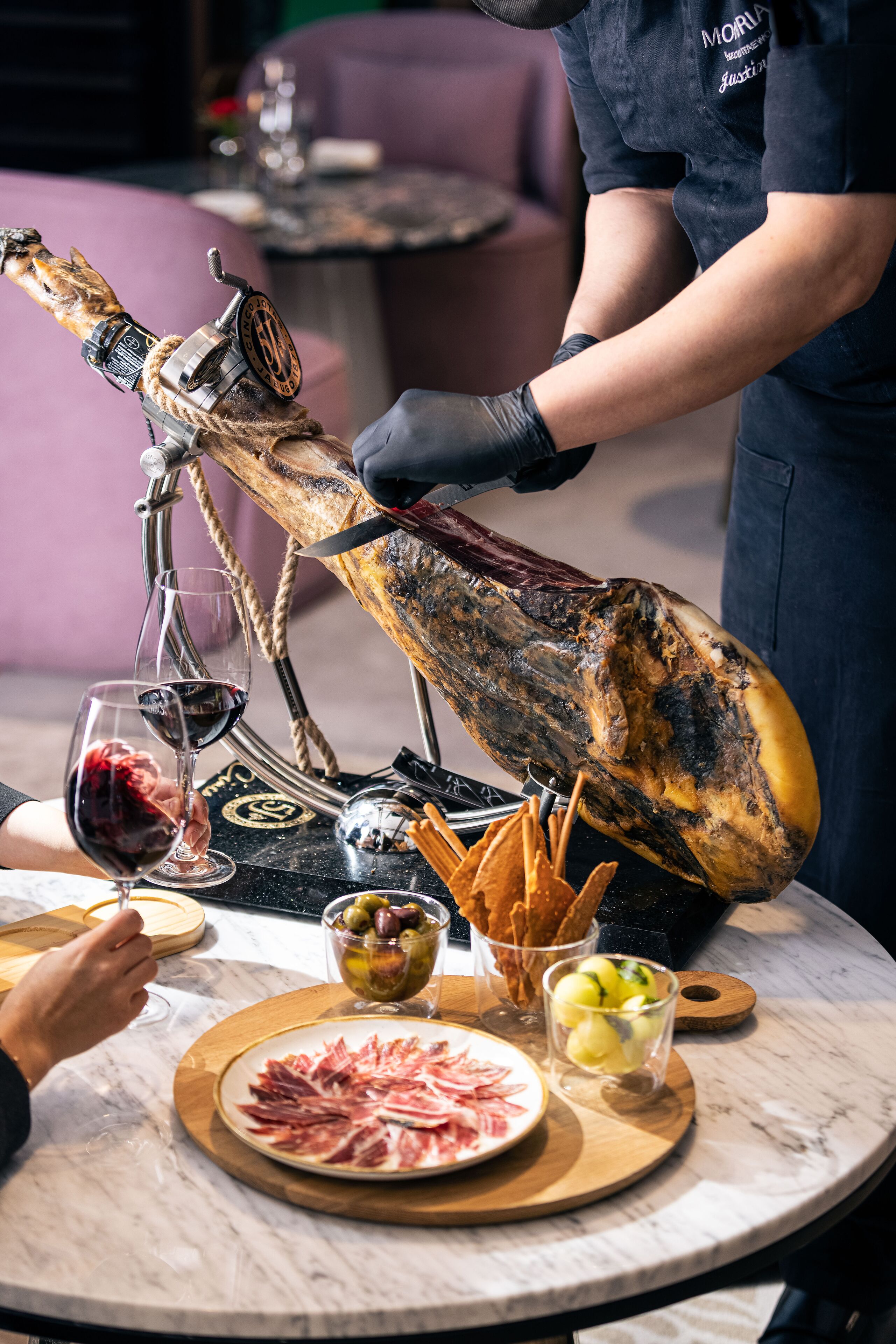 A charcuterie board with a large cured ham, wine glasses, olives, and bread.
