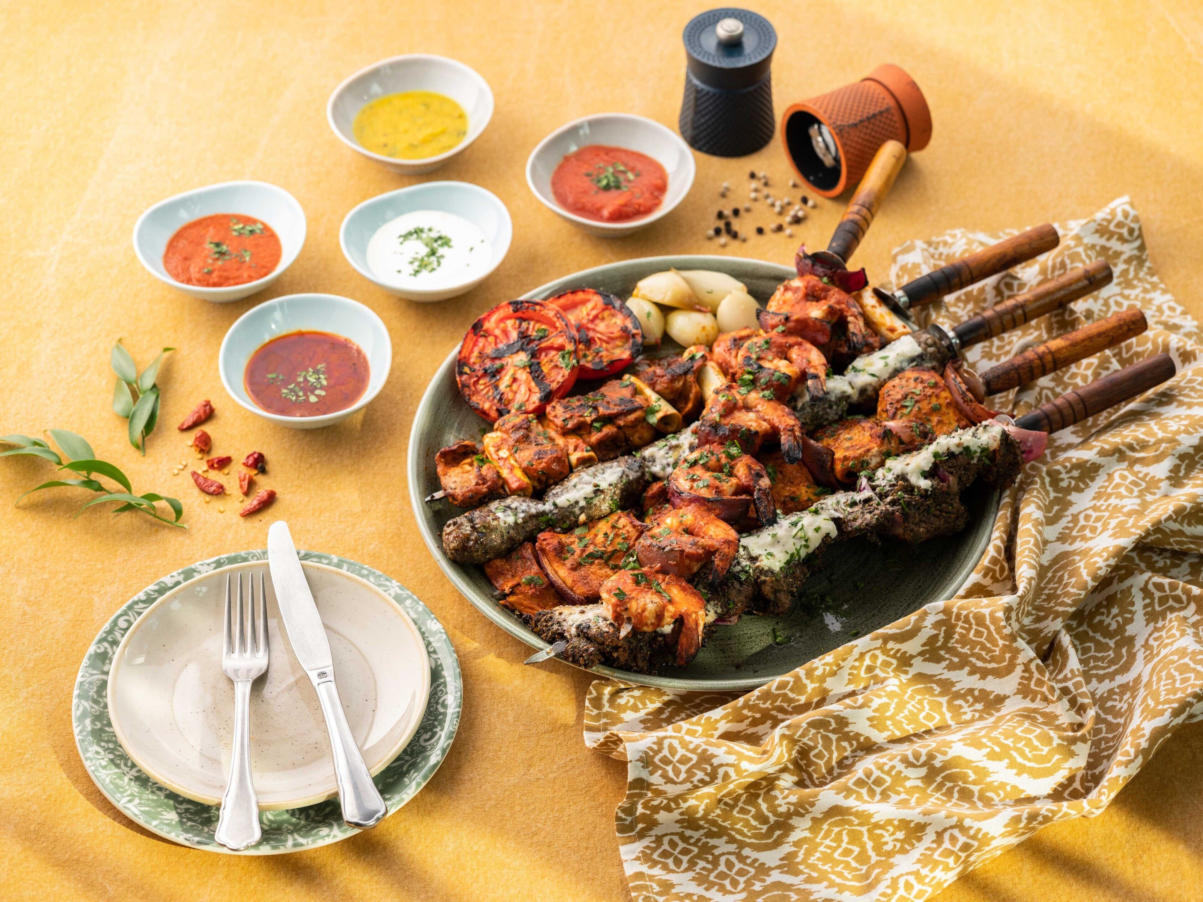 Un piatto di spiedini alla griglia con diversi tipi di carne e verdure, accompagnati da piccole ciotole di salse e condimenti.