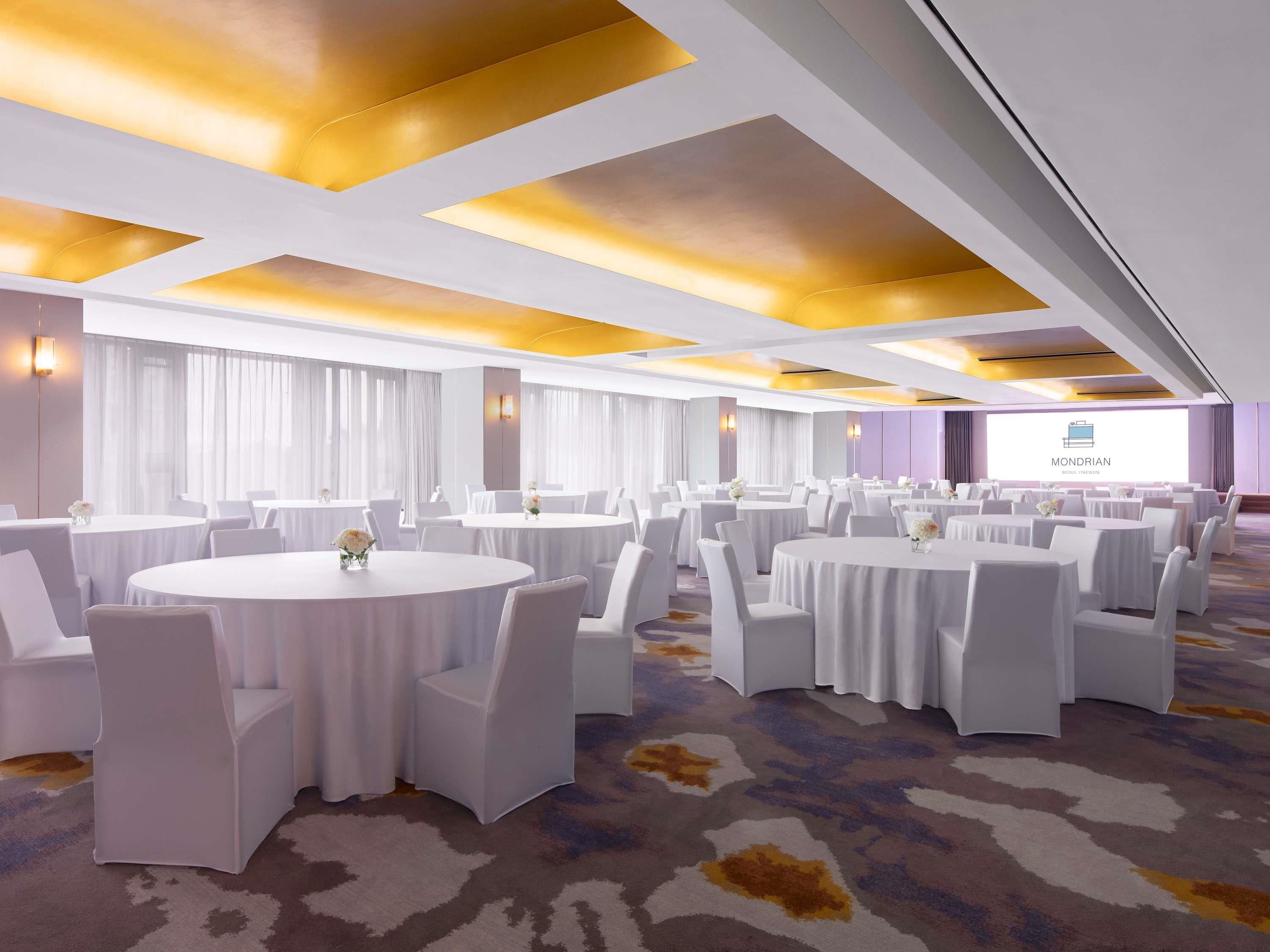 Une salle de conférence équipée de tables et de chaises rondes, d’un sol recouvert de moquette et d’un écran de présentation.
