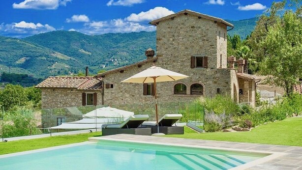A stone villa with a swimming pool, outdoor seating, and a mountainous backdrop.