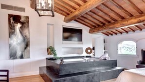A modern bathroom with a large sink, wooden beams, a TV, and a painting.