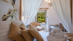 A bedroom with a bed, pillows, a nightstand, a window with curtains, and a painting on the wall.
