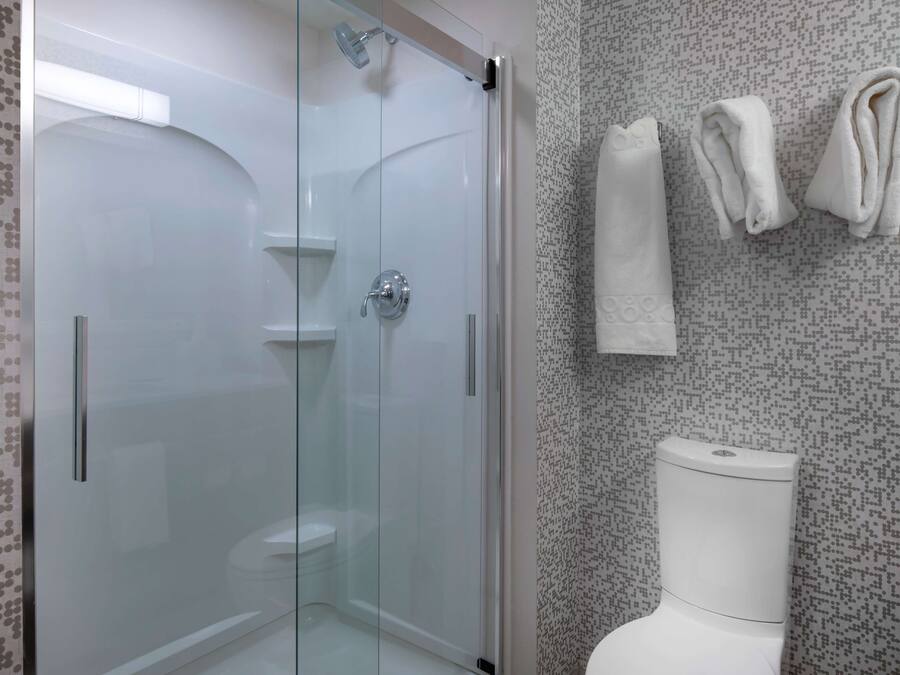 Ein modernes Badezimmer mit einer gläsernen Duschkabine, einer weißen Toilette und ordentlich gefalteten Handtüchern an der Wand.
