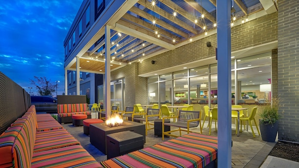An outdoor patio with a fire feature, seating, and a view of the restaurant inside. - Home2 Suites by Hilton Wayne, NJ (Wayne)