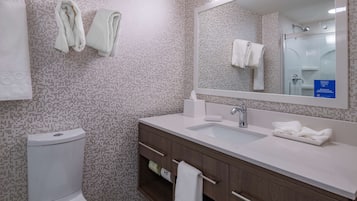 Un baño moderno con inodoro, lavabo y espejo. Hay toallas colgadas en la pared y un cartel que indica los servicios del hotel.