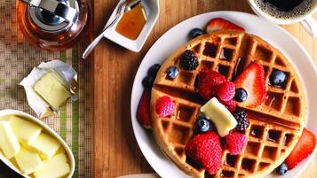 Une gaufre garnie de fraises, de myrtilles et de mûres, servie avec du beurre et du sirop.