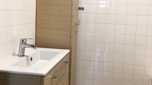 Baño con lavamanos blanco, mueble de madera y paredes con azulejos.