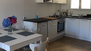 Una cocina moderna con armarios blancos, microondas, estufa y cafetera. Hay una mesa de comedor con sillas y un florero con flores.