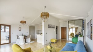 A spacious living room with a blue sofa, yellow armchair, and a glass coffee table. There is a dining area with a white table and chairs, and a kitchen in the background. - Tivat Montenegro (Tivat)