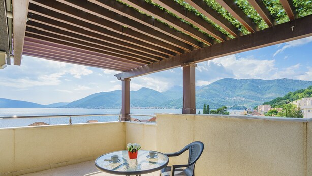 A balcony with a table and chairs, overlooking a scenic view of mountains and a body of water. - Tivat Montenegro (Tivat)