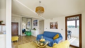 A living room with a glass coffee table, a blue sofa, a yellow armchair, and a wooden door leading to a balcony. - Tivat Montenegro (Tivat)