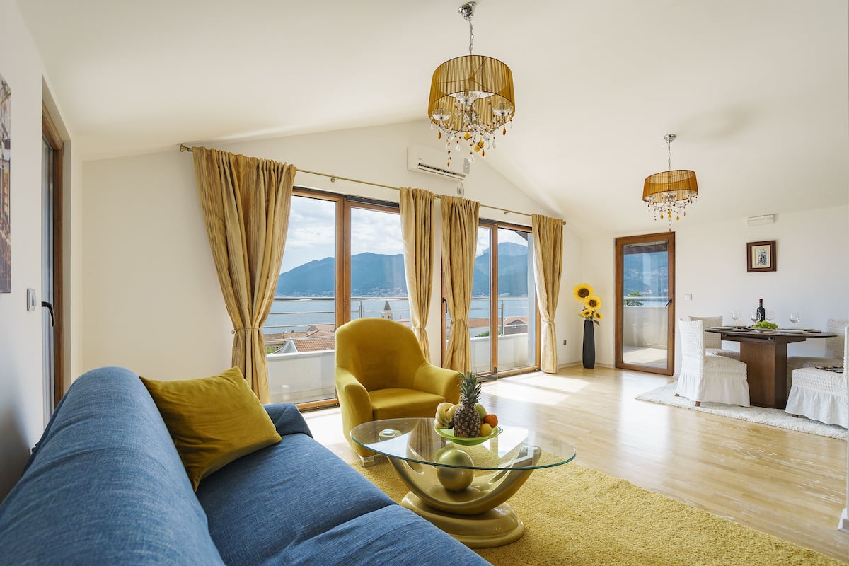 Uma sala de estar moderna com um sofá, uma mesa de centro de vidro, uma poltrona amarela e um espaço de refeições com mesa e cadeiras.
