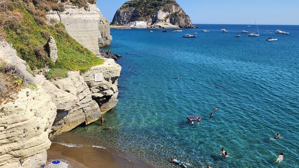 Une zone côtière caractérisée par une eau bleue et limpide, des falaises rocheuses et la présence de bateaux.