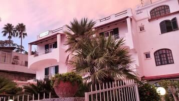 A multi-story building with balconies, a large potted plant, and a gated entrance.