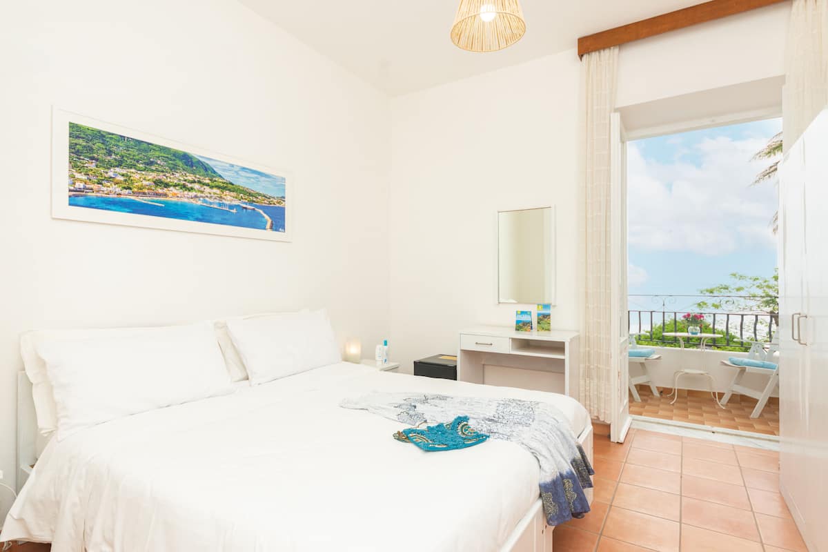Ein Schlafzimmer mit Bett, Schreibtisch, Stuhl und einem Balkon mit Meerblick.