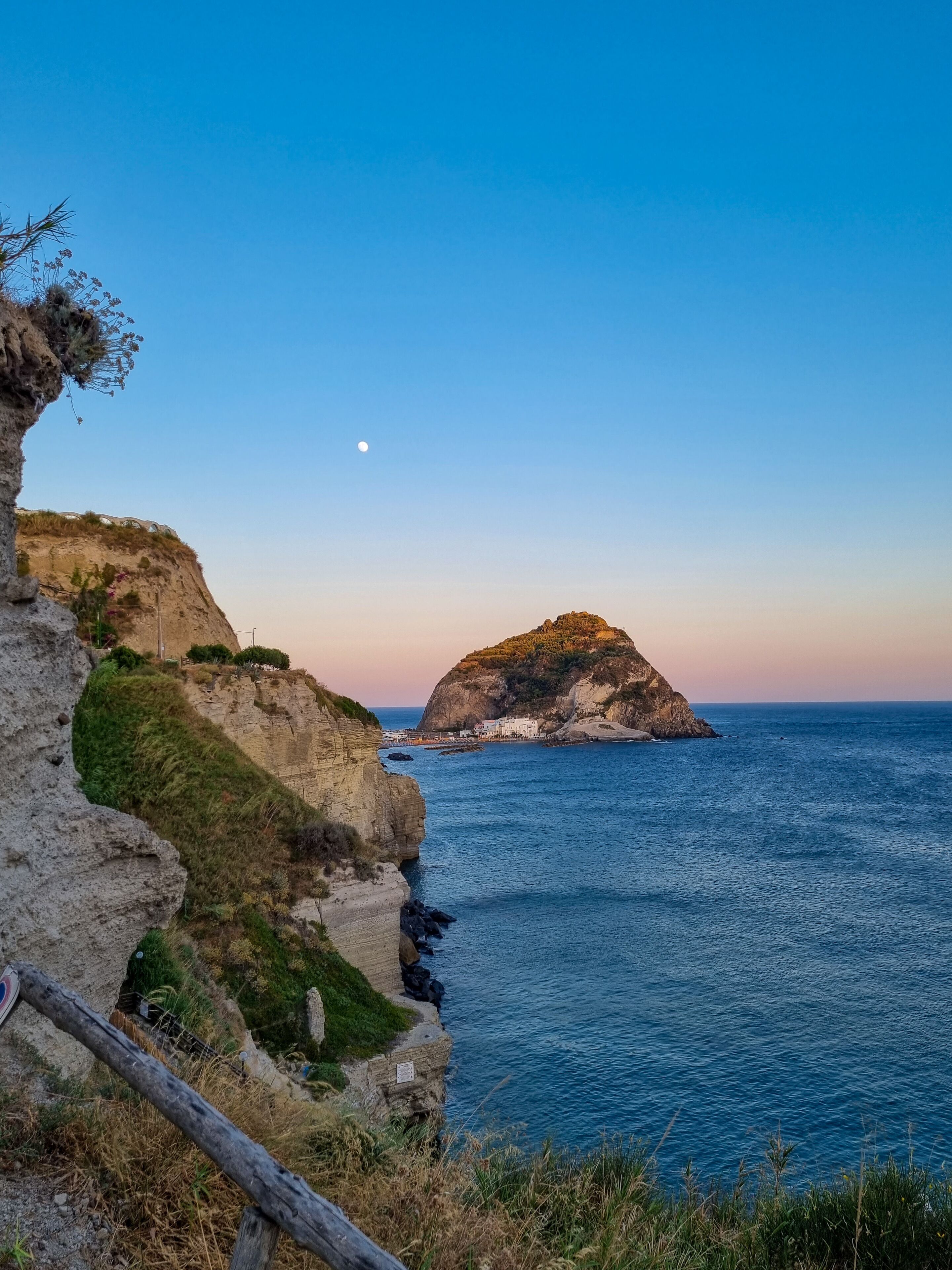 A coastal landscape with a prominent cliff and a small island in the distance.